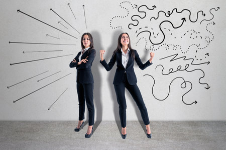 Two attractive young european businesswomen with drawn arrows standing in concrete interior. Direction, success, challenge and teamwork conceptの写真素材