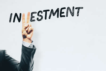 Hand with peace sign gesture replacing letter V in investment word on white background with mock up...