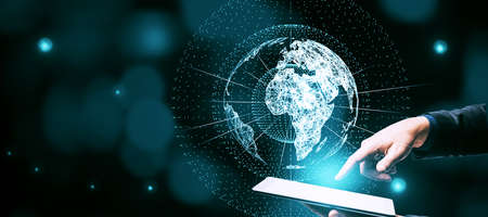 Businessman hand pointing at tablet with glowing globe hologram on blue bokeh background with mock up place. Digital interface and global innovationの写真素材