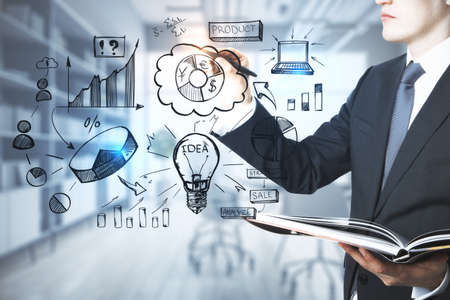 Attractive young european businessman drawing creative hand drawn business sketch on blurry office interior background. Training, idea, targeting and success conceptの写真素材