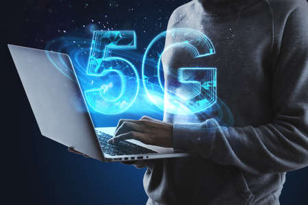 Hacker hands using laptop with creative glowing polygonal 5G hologram on blue background. Internet...