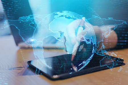 Close up of hands at desktop using pad with creative glowing globe interface on dark background....