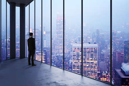 Businessman in empty office looking out of panoramic window with bright city downtown view. Future, tomorrow, perspective and career conceptの写真素材