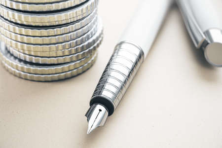 Close up of expensive classic pen and stacked silver coins on white desktop background. Finance and accounting concept. 3D Renderingの写真素材