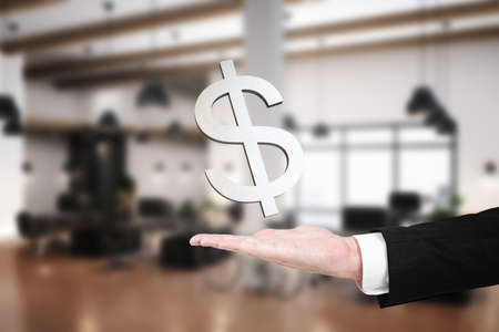 Close up of businessman holding abstract dollar sign on blurry office interior background. Finance,...