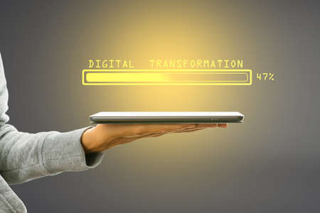 Hand holding tablet with abstract glowing loading bar on gray wall background. Digital transformation, internet, progress and technology conceptの写真素材