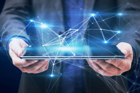 Close up of businessman hand holding tablet with abstract polygonal mesh on dark blue background....