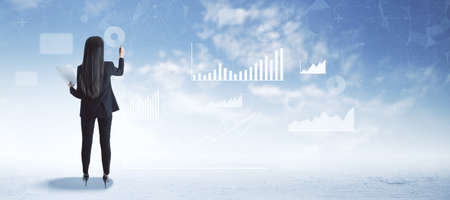 Back view of attractive young european businesswoman in suit standing on abstract blue sky with clouds background with business chart and graph. Finance, training, workshop and success conceptの写真素材