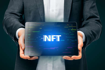Close up of man hands holding tablet with creative glowing NFT hologram on dark background. Non-fungible token and cryptocurrency conceptの写真素材