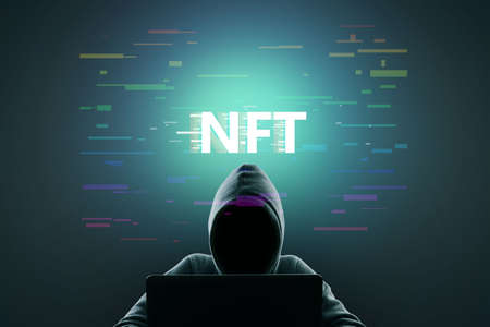 Hacker using laptop with creative glowing NFT hologram on dark background. Non-fungible token, hacking and cryptocurrency conceptの写真素材