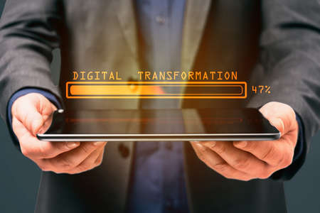 Businessman hand holding tablet computer with abstract glowing loading bar on gray wall background. Digital transformation, internet, progress and technology conceptの写真素材