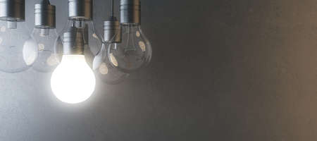 Glowing light bulb on blurry wide concrete wall background. Idea, innovation, solution and invention...