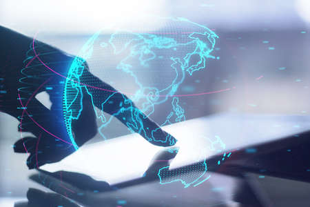 Close up of hand using tablet at desktop with glowing digital blue globe hologram on blurry...