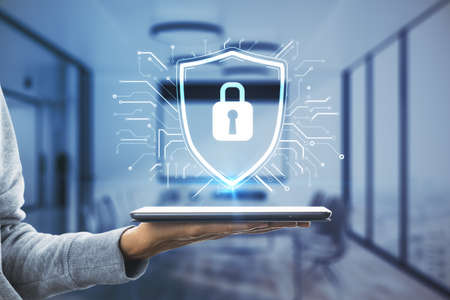 Close up of hand holding tablet with glowing padlock hologram in blurry office interior. Protection,...