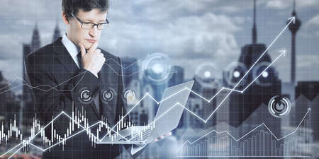 Attractive young european businessman using laptop computer with glowing business chart grid on...