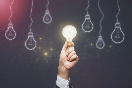 Businessman hand holding abstract light bulbs on dark background. Idea and innovation conceptの写真素材