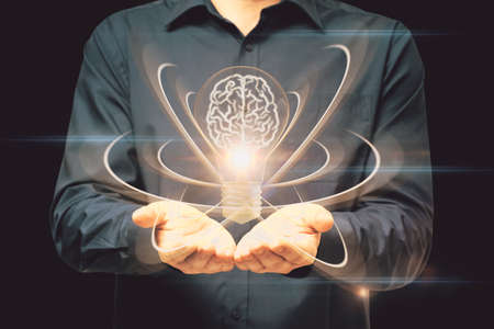 Close up of male hand holding abstract light bulb on dark wide background with digital brain and...