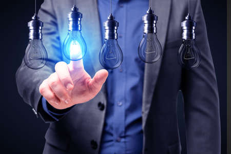 Close up of businessman hand pointing at abstract glowing row of light bulbs on dark background. Idea, solution and innovation concept.の写真素材
