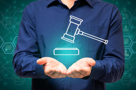 Close up of businessman hand holding creative digital gavel on glowing background. Online auction and technology conceptの写真素材
