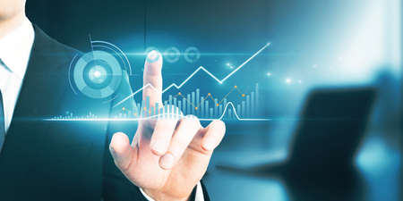Close up of businessman hand pointing at abstract glowing business chart on blurry background with...