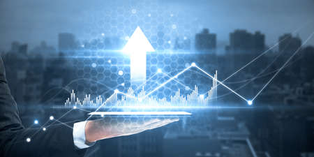 Close up of male hand using tablet with creative glowing arrow with business chart on blurry city background. Growth and investment concept. Double exposureの写真素材