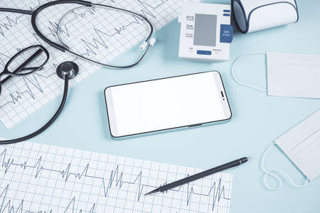 Top view of blue table with blank cellphone, stethoscope, cardiogram, pen, other items and mock up place. Doctor's office, workplace and diagnosis concept. 3D Renderingの写真素材