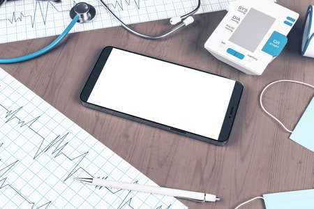Close up of wooden desk top with blank clean cellphone, stethoscope, cardiogram, pen, other items...
