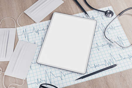 Top view of wooden desktop with empty tablet, stethoscope, cardiogram, pen, other items and mock up...