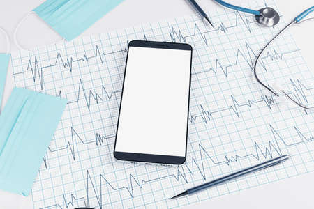 Top view of white desktop with empty smartphone, stethoscope, cardiogram, pen and mock up place. Doctor's office, workplace and diagnosis concept. 3D Renderingの写真素材