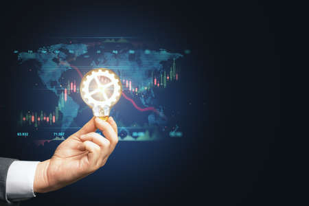 Close up of businessman hand holding lamp with glowing cogwheel with map, forex chart and mock up...
