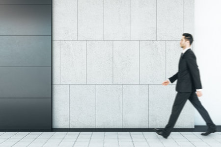 Businessman walking in abstract interior with empty mock up place on concrete tile wall and floor. Exhibition and art conceptの写真素材