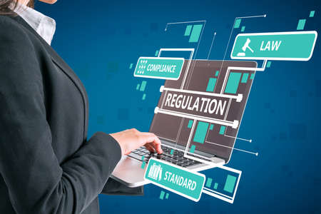 Close up of businesswoman hand using laptop with abstract digital regulation sketch or hologram on blue wall background. Compliance, management and law conceptの写真素材