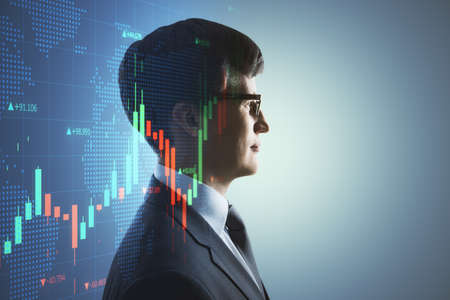 Portrait of attractive young european businessman thinking about candlestick forex graph and map on gray background with mock up place. Trade, economy and growth concept. Double exposureの写真素材