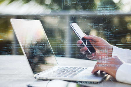 Close up of businessman hands using laptop and smartphone with creative glowing coding big data interface on blurry outdoor background. Technology and futuristic network. Double exposureの写真素材