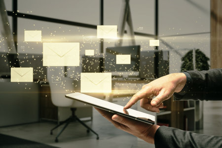 Close up of businessman hand pointing at tablet with creative glowing letters interface on blurry office interior background. E-mail networking and correspondence conceptの写真素材