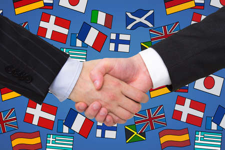 Close up of businessmen shaking hands with abstract colorful flag drawings. Travel, teamwork, union, translation and language learning conceptの写真素材