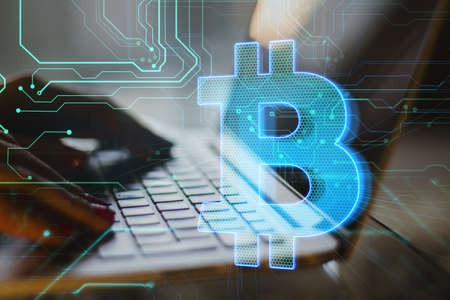 Close up of female hands using laptop with creative glowing blue bitcoin hologram on blurry circuit...