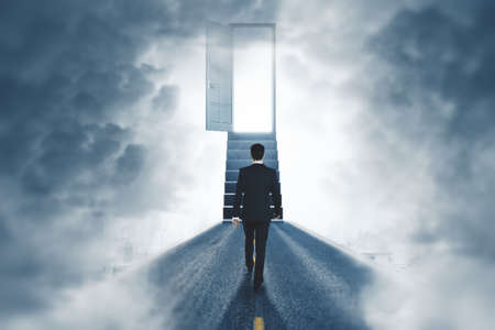 Back view of businessman walking towards open door and stairs in smoky room. Success, way, direction and happiness conceptの写真素材