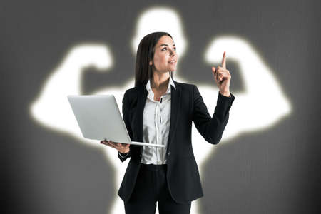 Attractive young european businesswoman with laptop and creative white muscle arms shadow on...