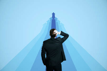 Back view of businessman looking at pink upward arrows on light background. Success, growth and...