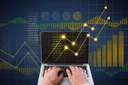 Close up of businessman hands using laptop with abstract glowing business chart hologram. Finance,...