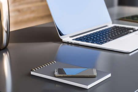 Close up of gray office desktop with smartphone, notepad and laptop with blurry mock up place on...