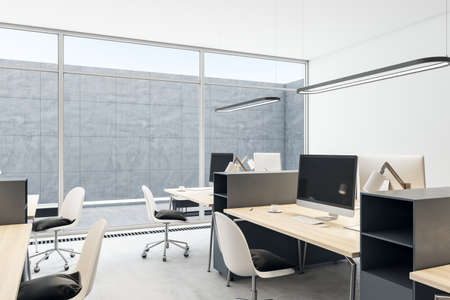 Clean coworking office interior with empty computer monitors on wooden desks, equipment, furniture and panoramic windows with daylight. 3D Renderingの写真素材