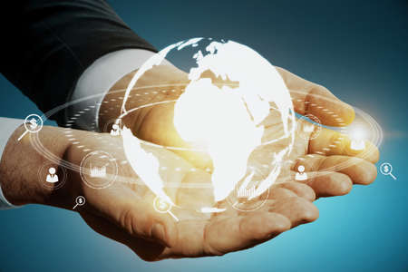 Close up of businessman hands holding glowing social globe hologram on blue background. Information,...