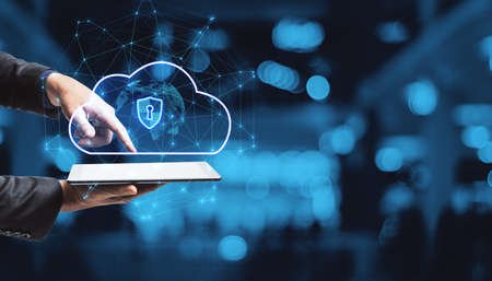 Close up of businessman hand pointing at tablet with abstract glowing cloud hologram with globe and safety icons, polygonal mesh on bokeh interior background with mock up place. Big data, information, computing and database concept. double exposureの写真素材