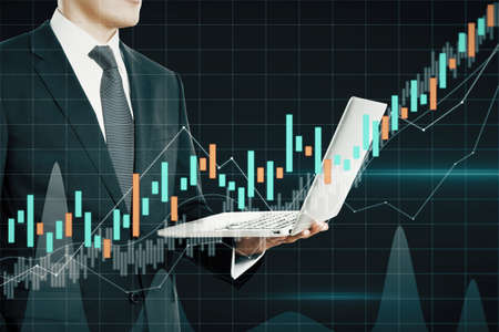 Attractive european businessman holding laptop with dark candlestick forex chart on blurry grid...