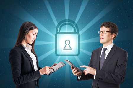 Attractive young european businesspeople using devices with glowing padlock on blue coding...