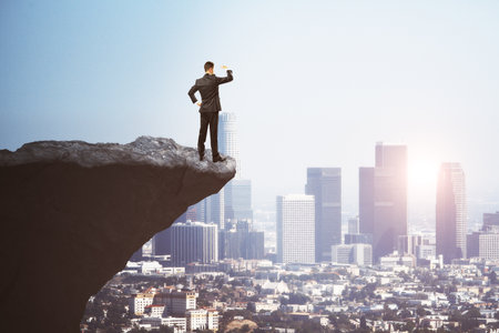 Attractive young european businessman on cliff edge looking into the distance on bright city...