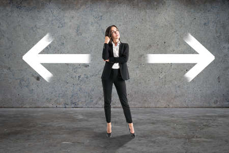 Attractive young european businesswoman with two arrows in concrete interior. Different direction and choice conceptの写真素材