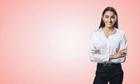 Business success concept with young smiling woman folded her hands in white shirt on abstract light pink background with copyspace for your or text, mockupの写真素材